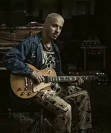 Watt seated with an electric guitar, surrounded by studio equipment