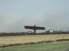 Statue viewed in the distance across fields. Railway overhead power lines can be seen in the immediate foreground