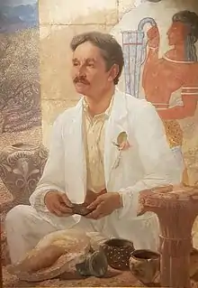 Painting of a man, holding something (a potsherd or Linear B tablet) in his hands, seated looking into the distance: a Minoan fresco is visible behind him.