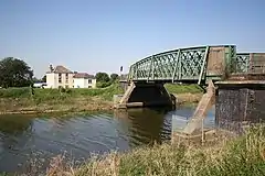 Rivetted steel railway-era carries a narrow road over the river Welland into the town from the west
