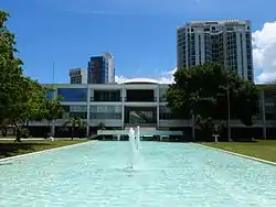 Photograph of the Supreme Court Building, a bright white building of two stories with an open space below, overtopped by a shallow dome