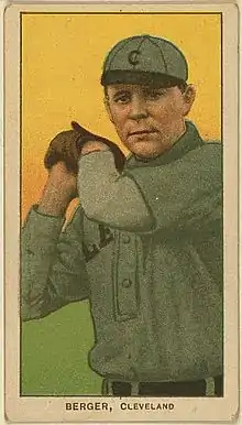 A baseball card of a man wearing a gray baseball uniform with a black "C" on the cap holding his hands raised–the side of his head wearing a baseball glove on his left hand.