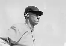 A man wearing a baseball cap and jersey devoid of any markings looks–the right.