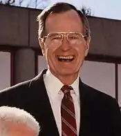 George H.W. Bush, outside in a black suit and eyeglasses, smiling