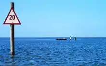 A small boat and wading fishermen in shallow water by a beach