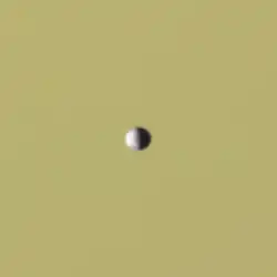 A small, half-illuminated ellipsoidal object in front of Saturn as a backdrop