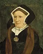 A Tudor woman wearing a simple gable hood. She also wears a black gown and black partlet, underneath some furs