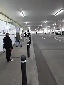 People queueing at an Irish supermarket, March 2020; strips of black tape on the ground to demarcate 2-metre gaps.