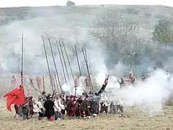 A colour photograph showing a re-enactment of a seventeenth century battle, with a unit of infantry firing muskets.