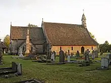 A church seen from the north with an extensive roof. On the right is the nave with a bellcote at the west end; on the left is the chancel with the vestry.