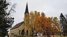 yellowish brick church with a spire partially obscured by autumn leafed trees