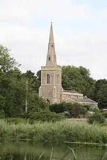 A stone church seen from the southeast, showing chancel, beyond which is a taller nave with a south aisle, and a tower with a spire