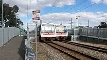 A station with two side platforms and a train at each platform viewed from the end of the trains