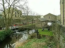 An urban beck; a stream with footbridge over it among several sandstone buildings